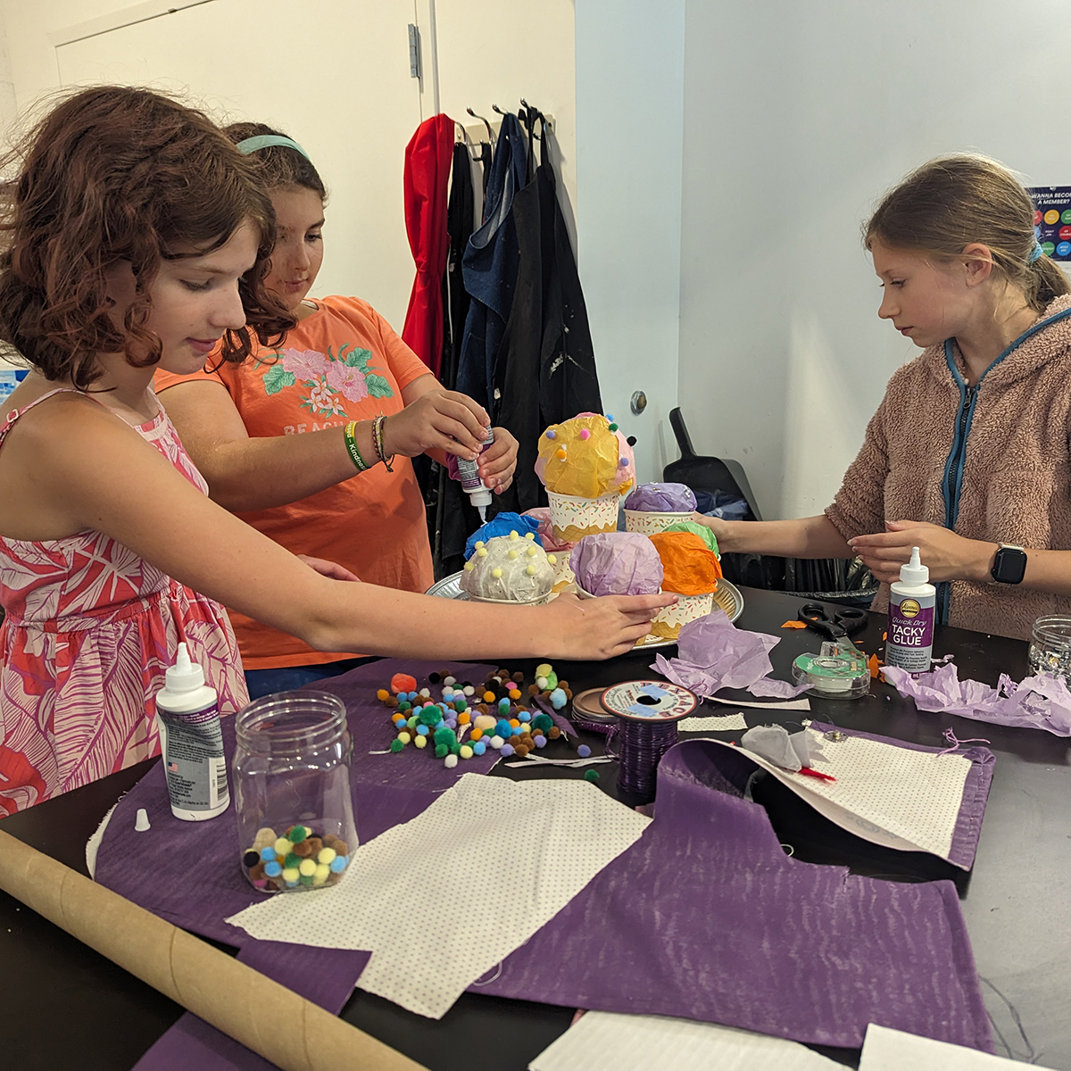 Youth education students creating a soft sculpture of cupcakes using colorful fiber materials, glue, and pom poms