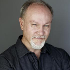 Voice Actor Dick Terhune, an older white man with a neat beard, wearing a black shirt